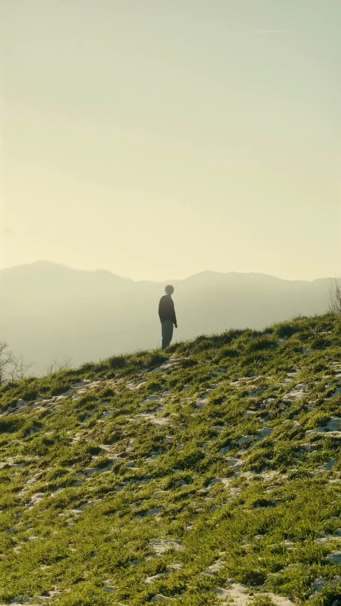 A lone figure standing in a sunlit hilly landscape