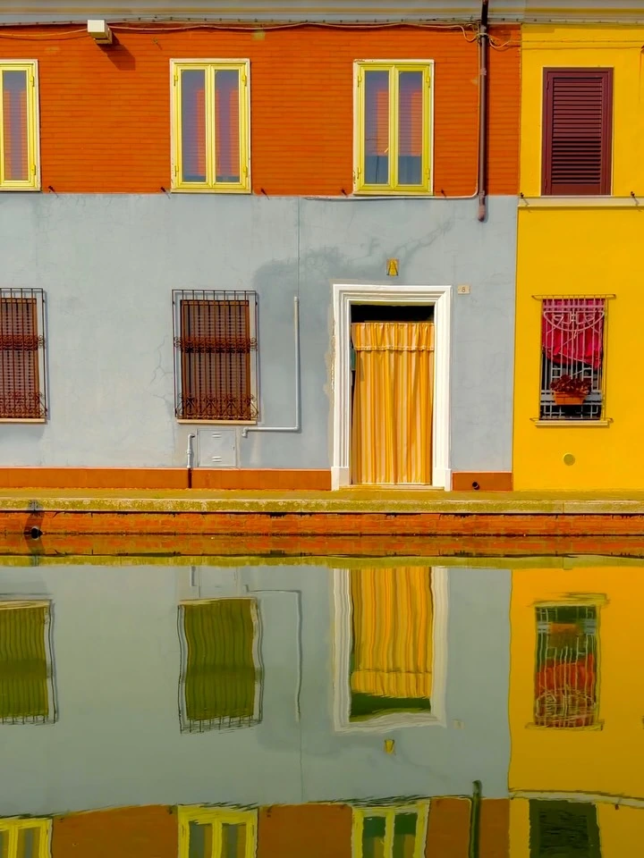 Yellow and red canal-side facades reflected in the water at Comacchio