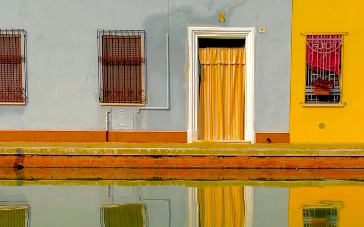 Yellow and red canal-side facades reflected in the water at Comacchio