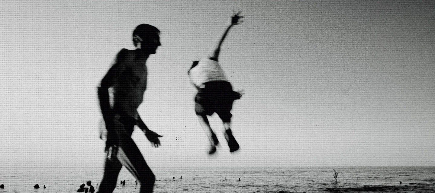 A figure suspended in a jump above the beach in black and white