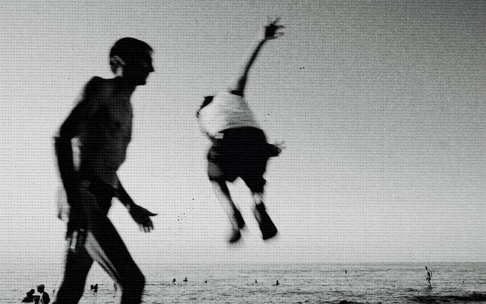 A figure suspended in a jump above the beach in black and white
