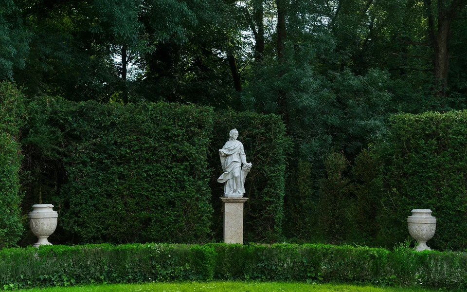 A white statue framed by clipped hedges and dark trees in the Parco Romantico
