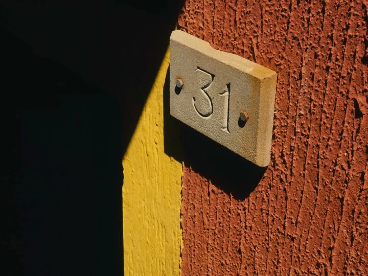 A ceramic number tile on a sunlit orange wall