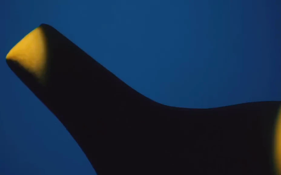 A sculptural dark chair shaped by yellow light against a blue background