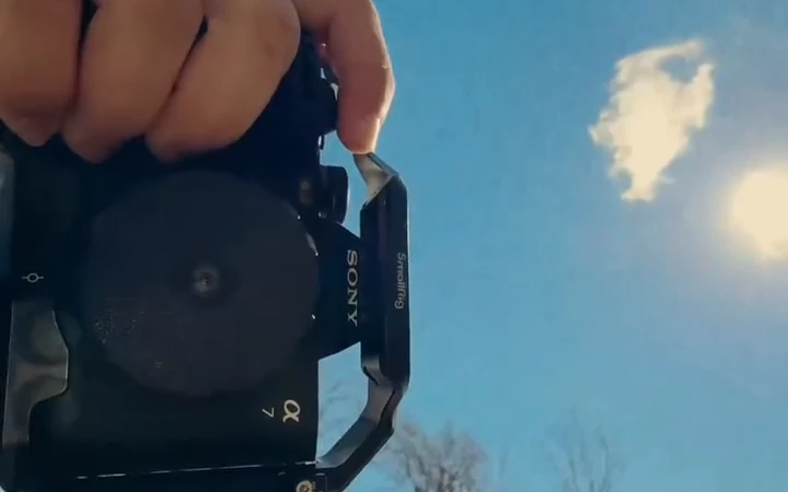 A camera fitted with a small lens, held against a blue sky