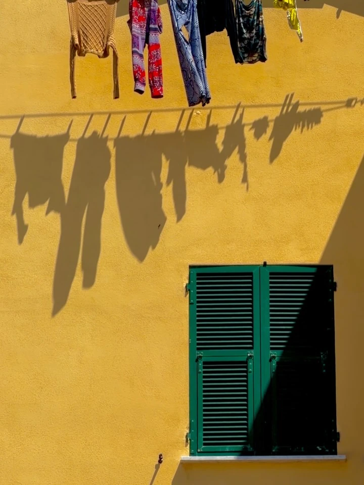 Shadows of hanging laundry above green shutters on a yellow wall in Recco