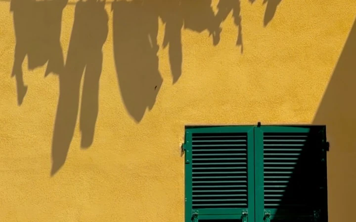 Shadows of hanging laundry above green shutters on a yellow wall in Recco