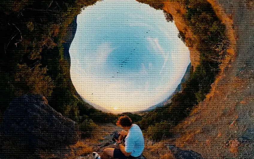 A person seated beneath a circular opening framing the blue sky