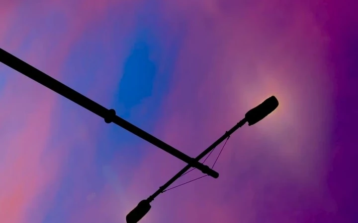 An inverted street lamp cutting diagonally across a violet and orange sky