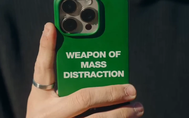 A green phone case held against a dark shirt, with the words Weapon of Mass Distraction