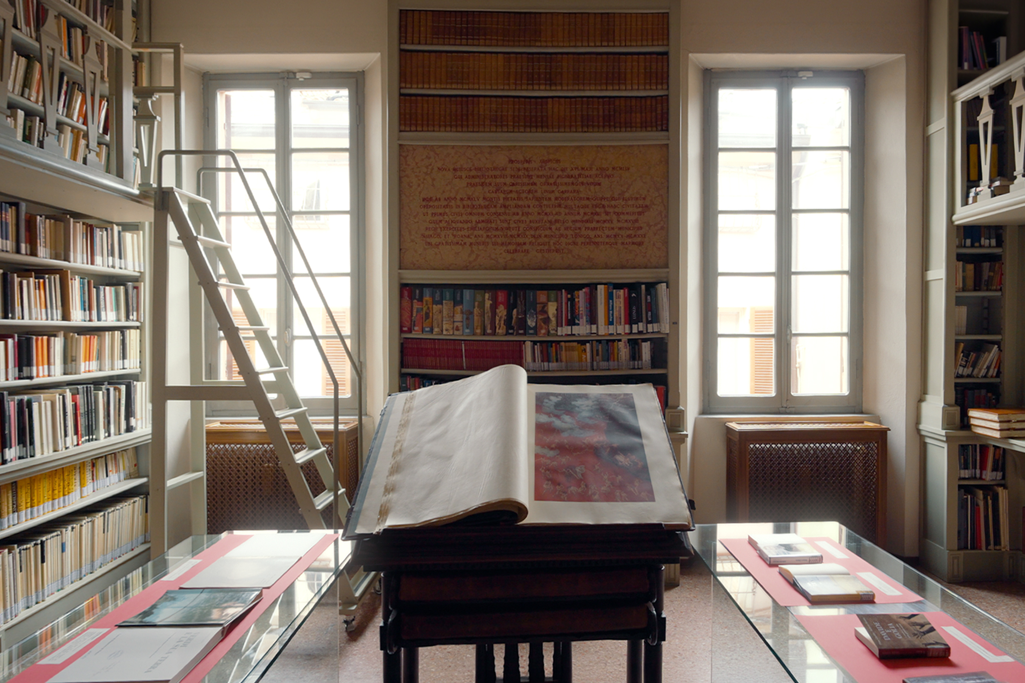 Bright library reading room with large illuminated manuscripts open on display tables